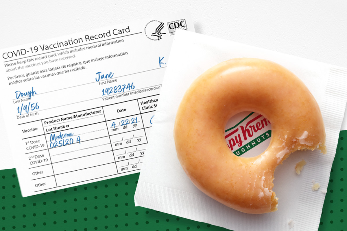 A glazed donut with a bite taken out of it sits on top of a Krispy Kreme napkin and a COVID-19 vaccination card filled out with the name “Jane Dough.”