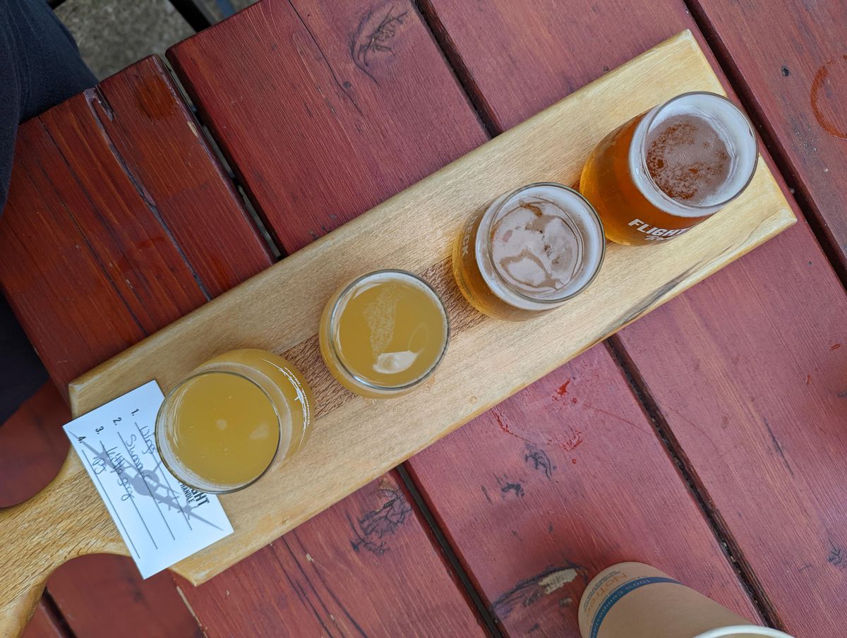 Four small pours of beer and a white card on a wooden board.