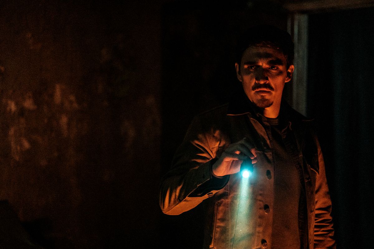 Joel (Kyle Gallner) stands in a dark, red-lit room holding a bright blue flashlight in Smile