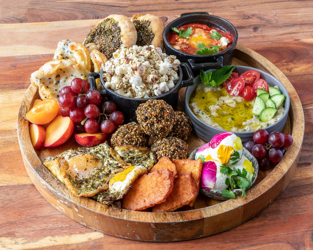 A mezze platter from Lulu Berkeley with a mix of house-baked breads, dips, spreads, and shareable items including&nbsp;Za’atar Fried Eggs, Fried Halloumi, Labneh, Baba Ganoush, Shakshuka, Za’atar Mana’eesh,&nbsp;seasonal fruit, and more.
