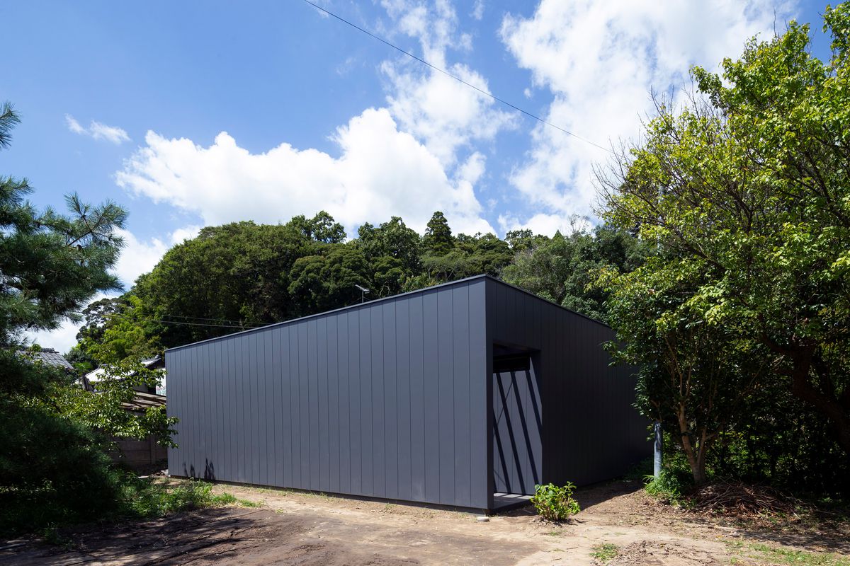 A black-colored boxy house is surrounded by trees.