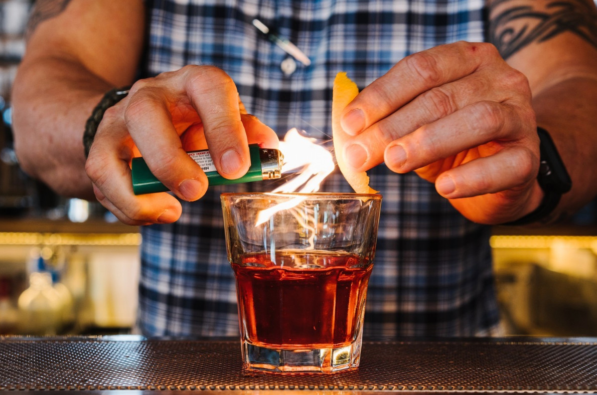 Someone torching an orange peel over a cocktail. 