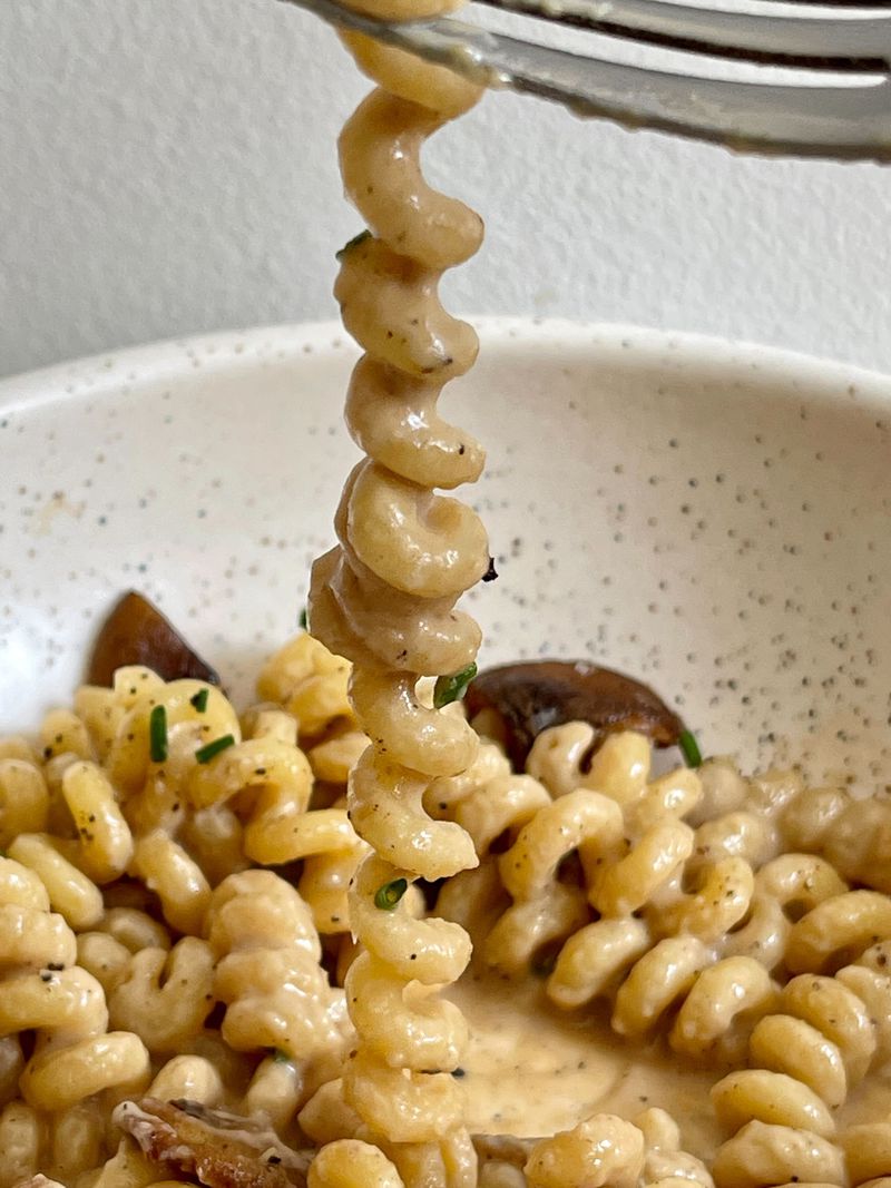 A coil-shaped pasta being stretched over a bowl of saucy pasta.