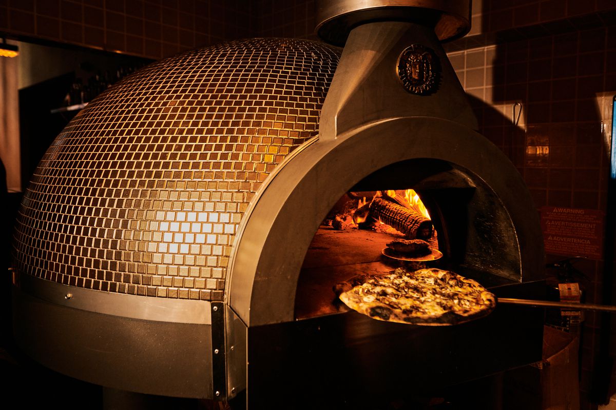 A mushroom pizza is shown being taken out of the fiery domed oven.