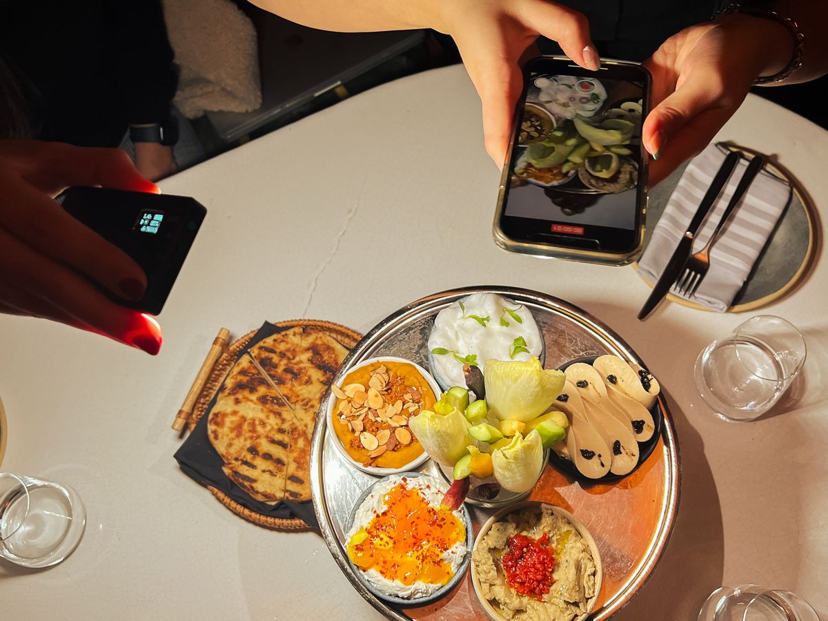 An iPhone and a handheld light hover over a platter of food at Zou Zou’s, a restaurant in Manhattan.