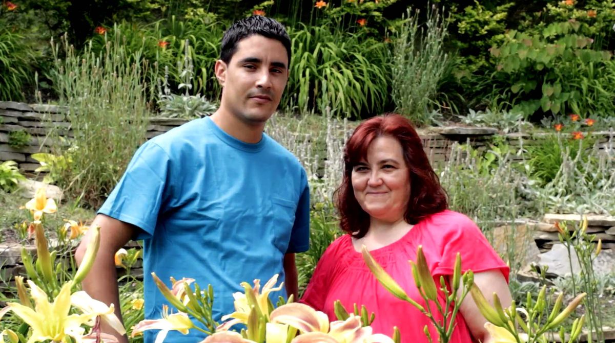 A young man and a middle-aged woman stand in a garden.