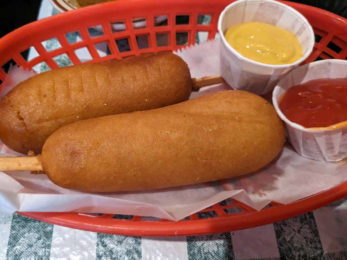 Two corndogs in a red plastic basket.