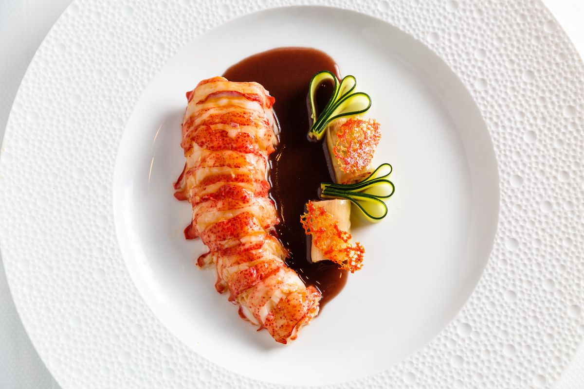 Speckled maine lobster tail sits next to leek cannelloni and dark brown red wine rosemary sauce