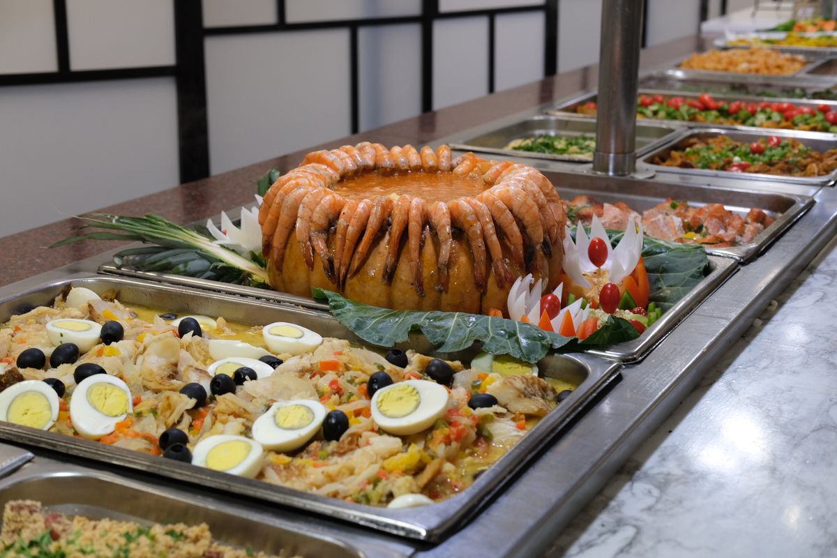 A buffet of hot chafing dishes containing camarão na moranga, or shrimp stew in pumpkin next to Portuguese salt cod stew called bacalhoada at Minas Emporium and Grill in Marietta, GA.