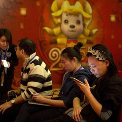 In this photo taken Monday, Feb. 2, 2015, a woman browses her smartphone near other attendees at a press conference in Beijing. China announced Wednesday, Feb 4. 2015 that users of blogs and chat rooms will be required to register their names with operators and promise in writing to avoid challenging the communist political system, further tightening control over Internet use. 