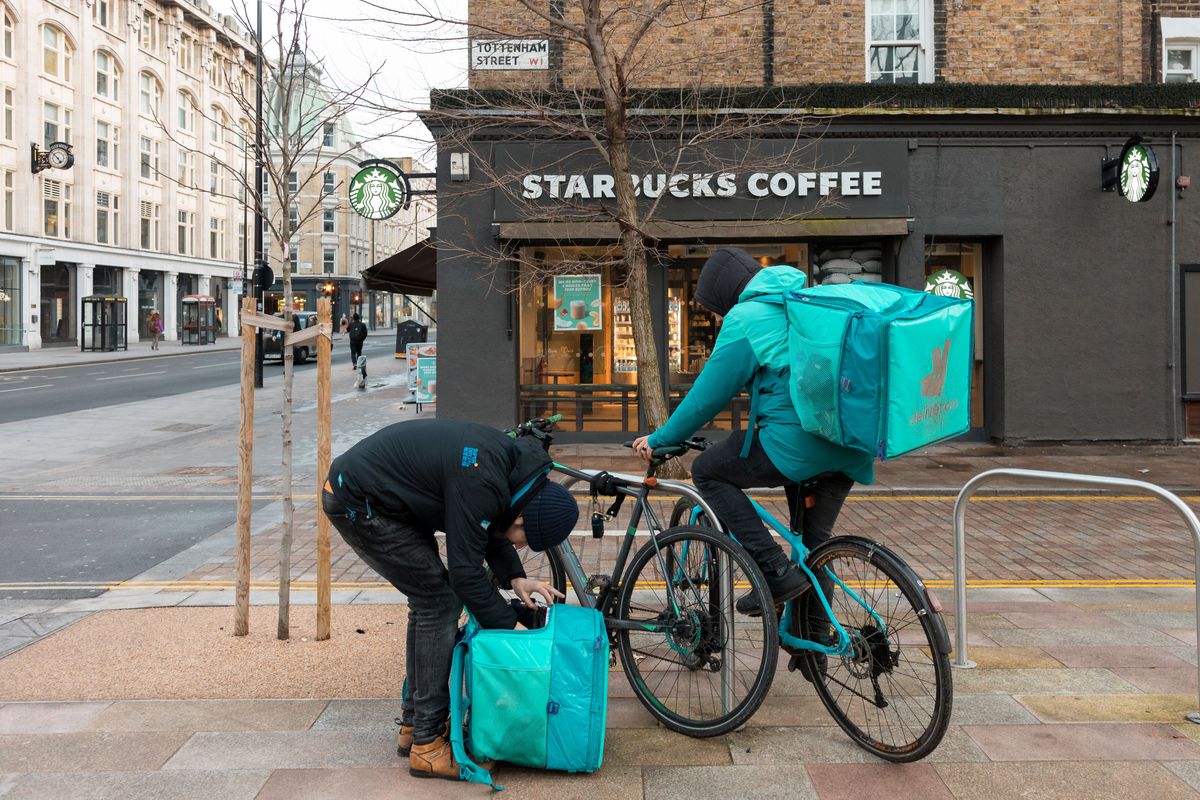 Two Deliveroo riders seen in front of a Starbucks coffee store in London