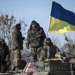 Ukrainian soldiers stand next to a Ukrainian national flag atop an armored vehicle near Artemivsk, eastern Ukraine, Monday, Feb. 23, 2015. A Ukrainian military spokesman says continuing attacks from rebels are delaying Ukrainian forces' pullback of heavy weapons from the front line in the country's east. 