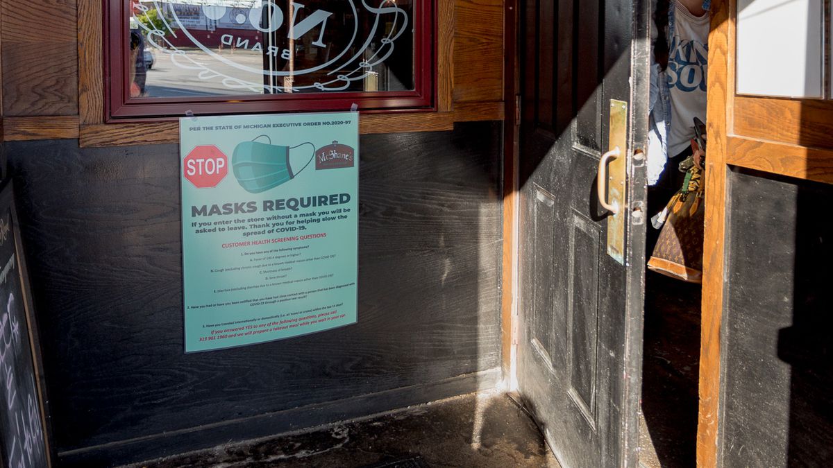 A woman walks out of the door at McShane’s next to a sign that warns about mask policies.
