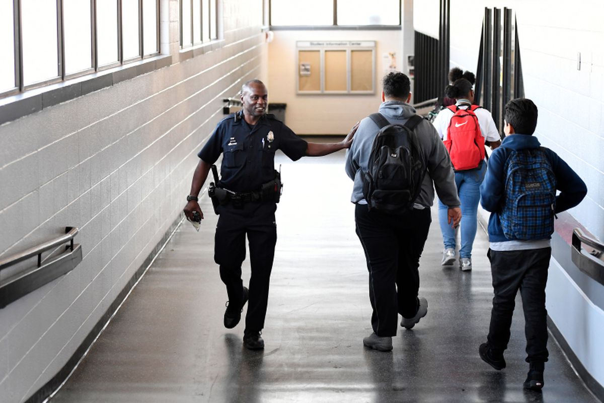 A smiling school police officer interacts with students in a hallway.