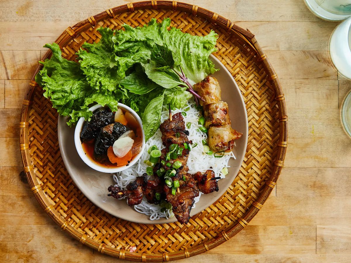 Bun cha, a barbecue platter featuring pork prepared three ways served with vegetables and rice noodles in a bamboo plate. 