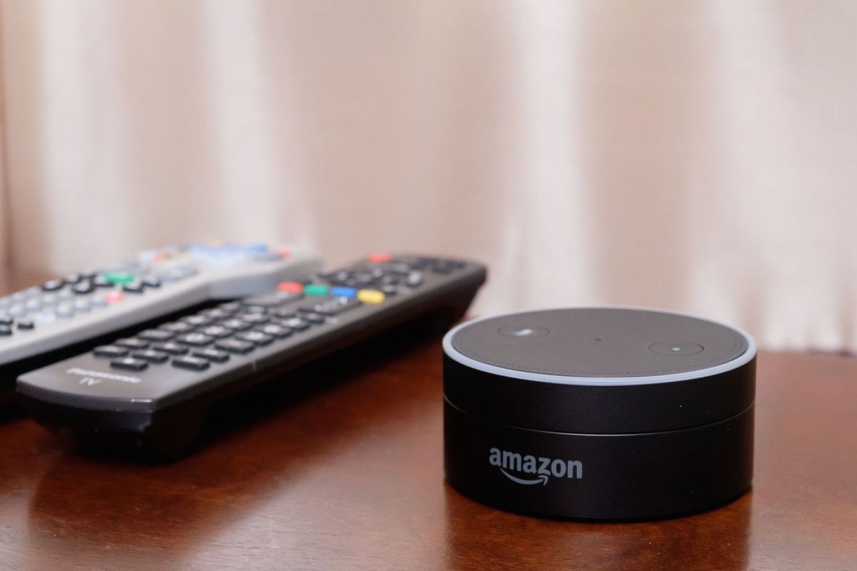 Amazon Echo Dot on a table beside a pair of TV remotes.