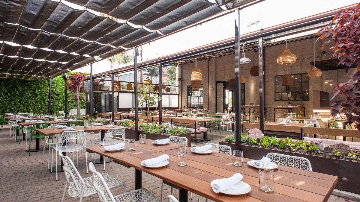 Covered patio with wood-top tables and white chairs, accented by green plants