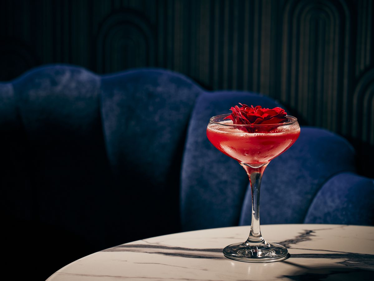 A red cocktail garnished with a red flower on a marble table.