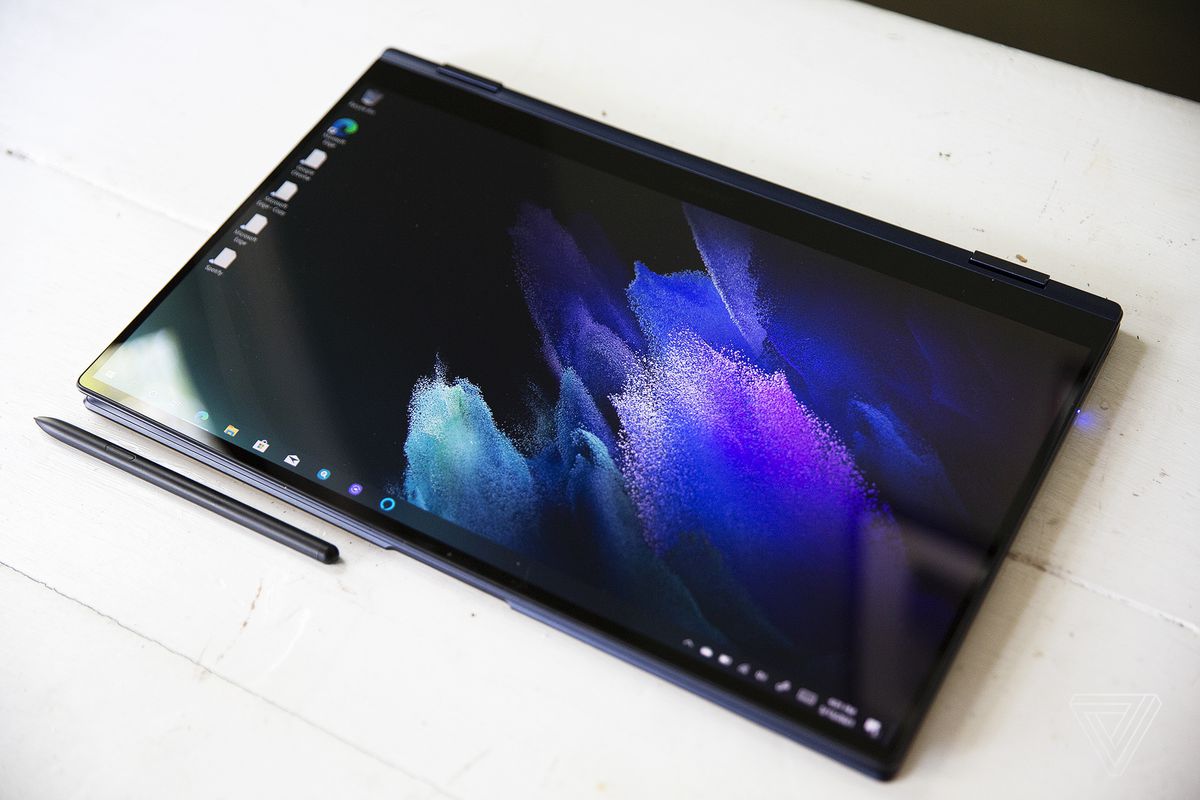 The Samsung Galaxy Book Pro 360 (15-inch) in tablet mode with the stylus below it on a white table. The screen displays a purple pastel pattern on a dark background.
