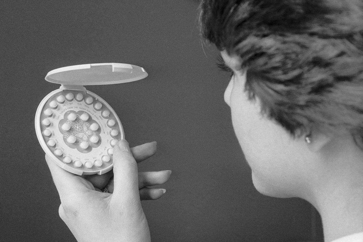 A woman holding and looking at an open circular pill dispenser.