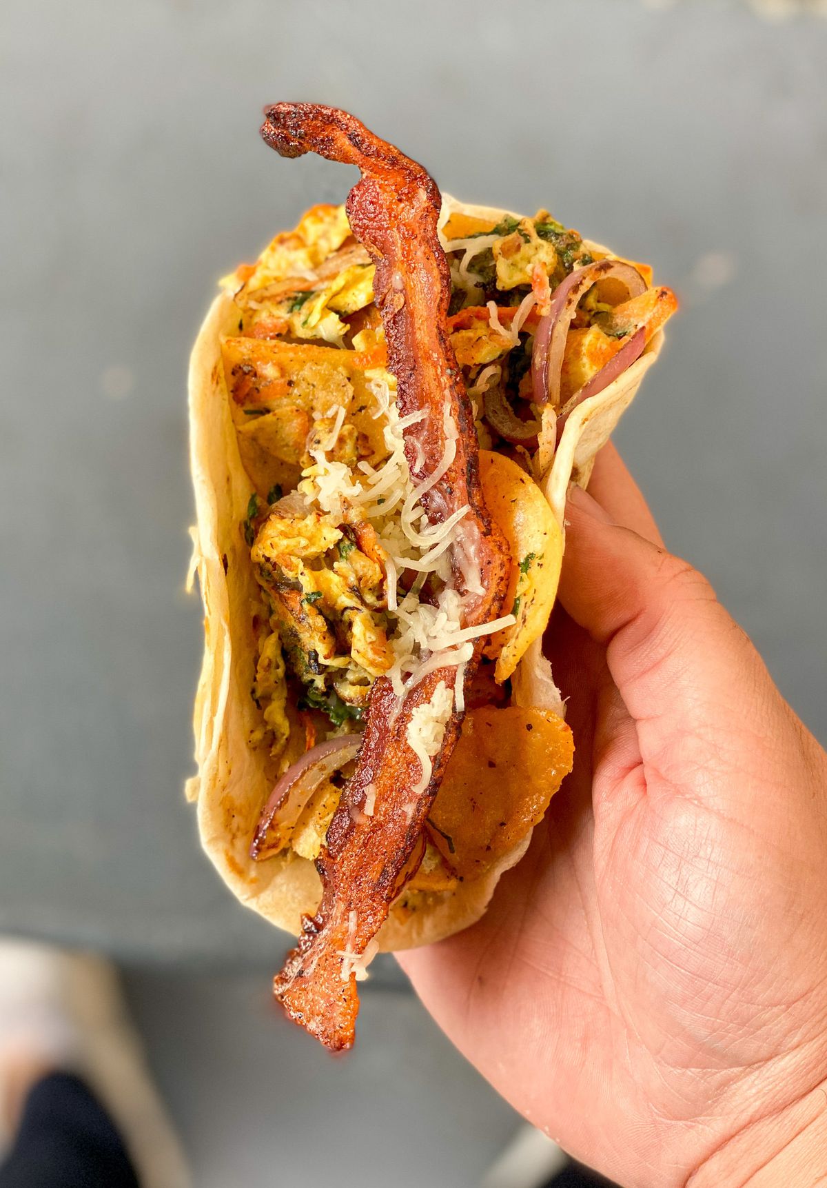 A hand holding a taco with a strip of bacon sticking out.