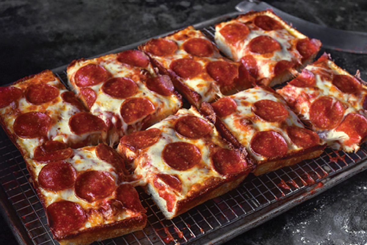 A rectangular pepperoni pizza is cut up into squares and rests on a wire rack in a pan