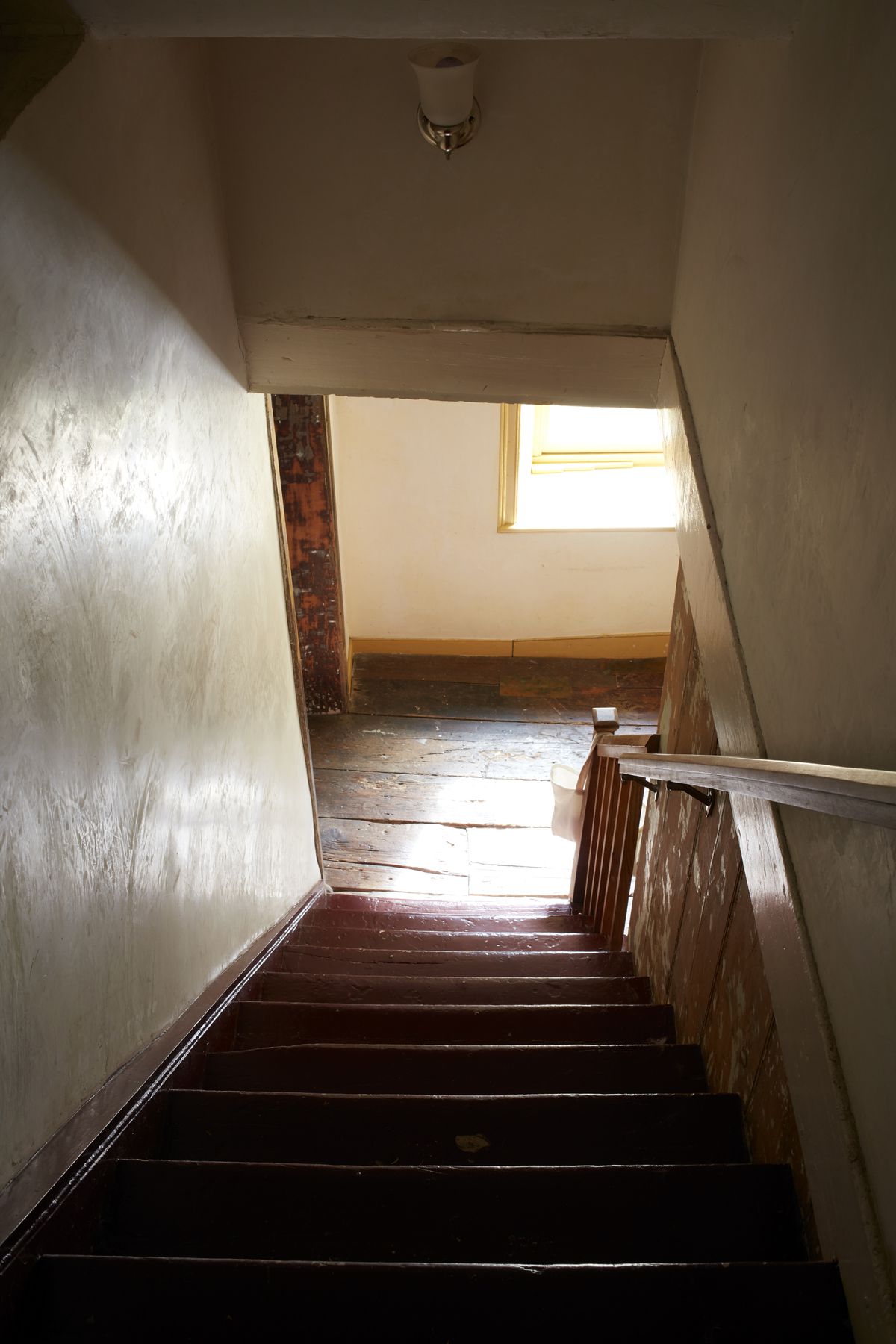 A shot that looks down a wooden stairway surrounded by white plaster walls.