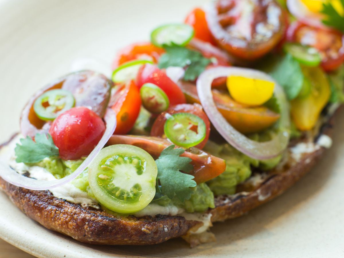 A piece of toasted thickly heaped with colorful cherry tomatoes cut in half, onions, and avocado.