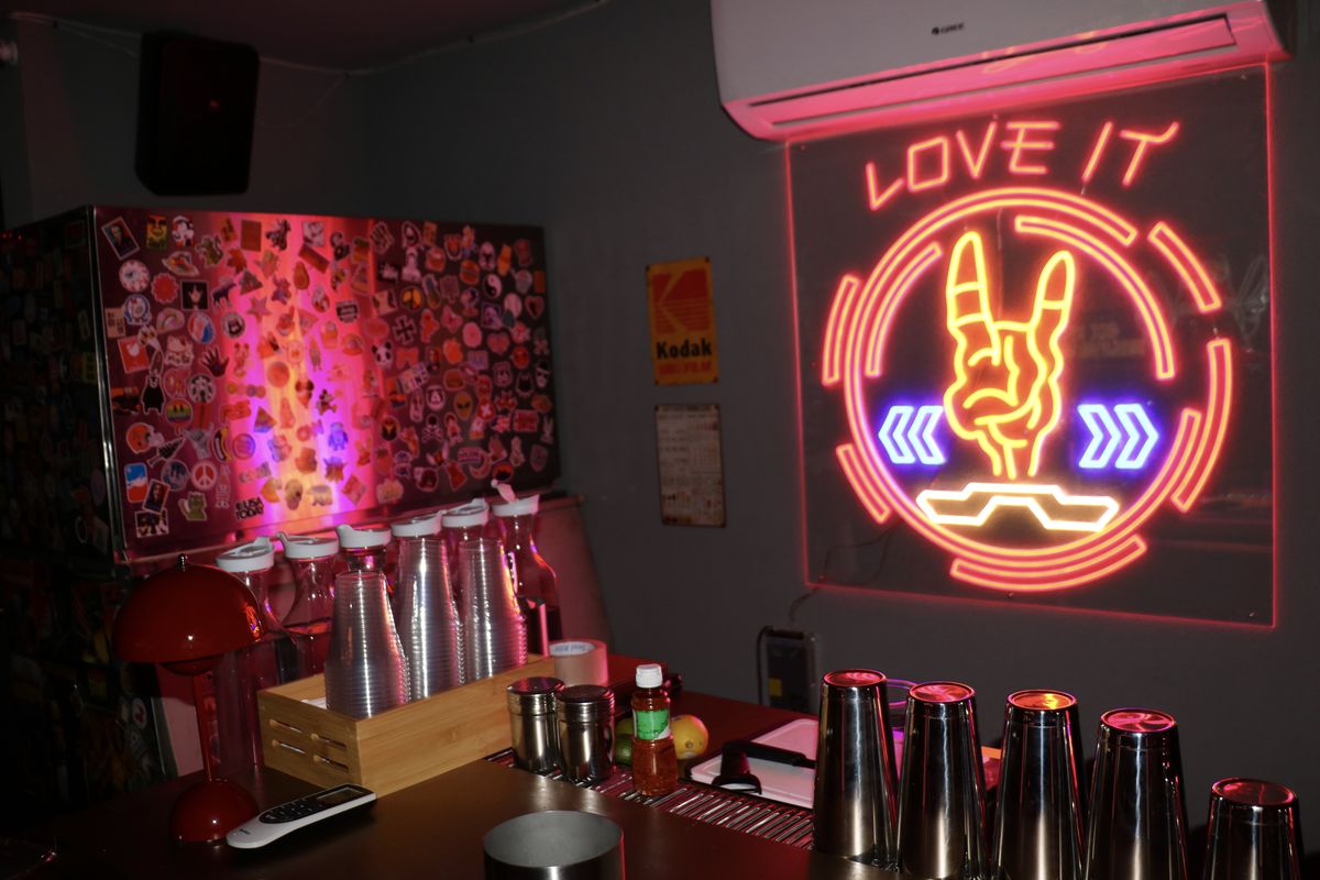 A neon sign with the words “Love It” behind a dark bar.