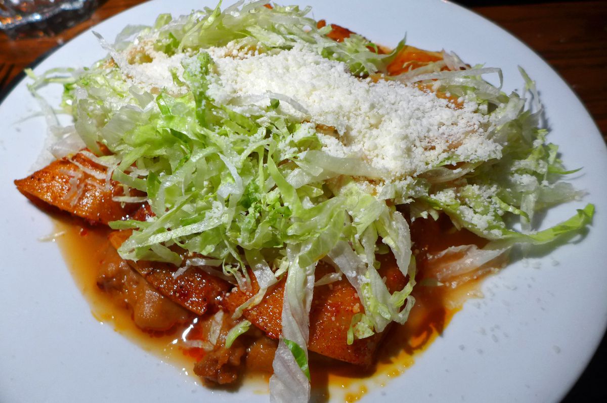 Three enchiladas in red sauce heaped with shredded lettuce and dried cheese.
