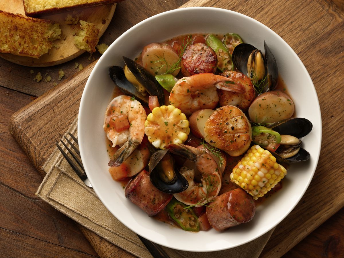 Overhead view of a white bowl full of sausage, pieces of corn on the cob, mussels, and shrimp