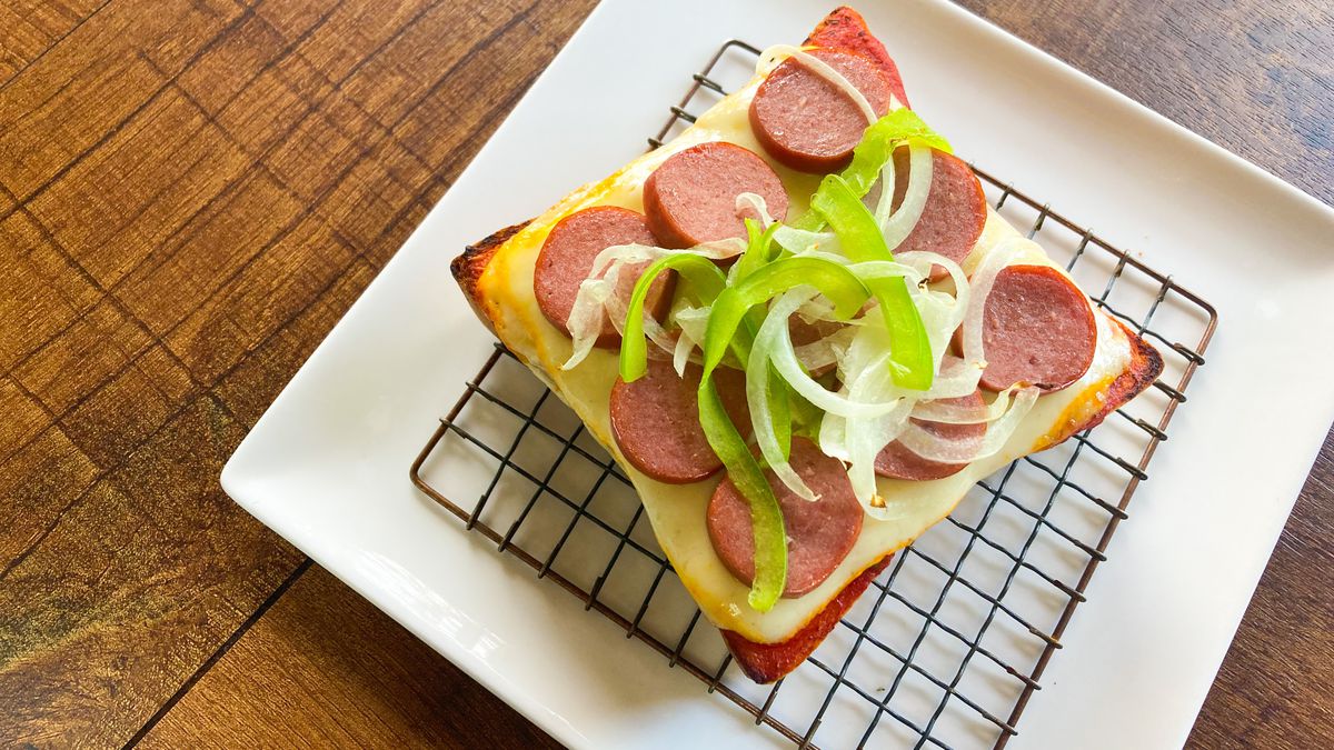 A square slice of shokupan comes topped with muenster, sliced hot dogs, thinly sliced green peppers and white onions, and tomato sauce. 