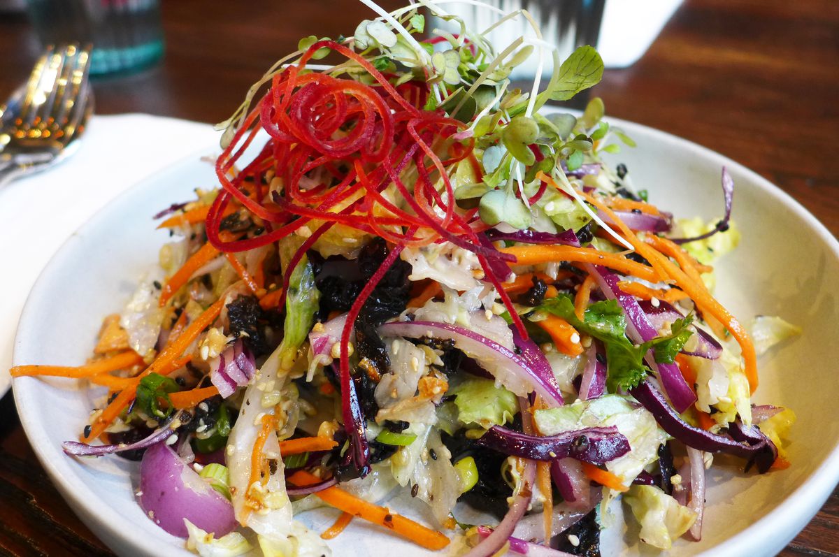 A conical pile of salad with dark tea leaves and shredded raw beet and carrot on top.