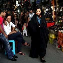 In this Tuesday, May 28, 2013 photo, an Iranian woman makes her way as two shopkeepers sit at left, at a bazaar in downtown Tehran, Iran. On the roughneck streets in south Tehran, paramilitary volunteers look to the most hard-line presidential candidate as the best defender of the Islamic system. On the other end of Tehran's social ladder, a university professor plans to snub next week's election. In between is a mix of splintered views, apathy and indecision based on dozens of AP interviews suggesting a still wide open race.