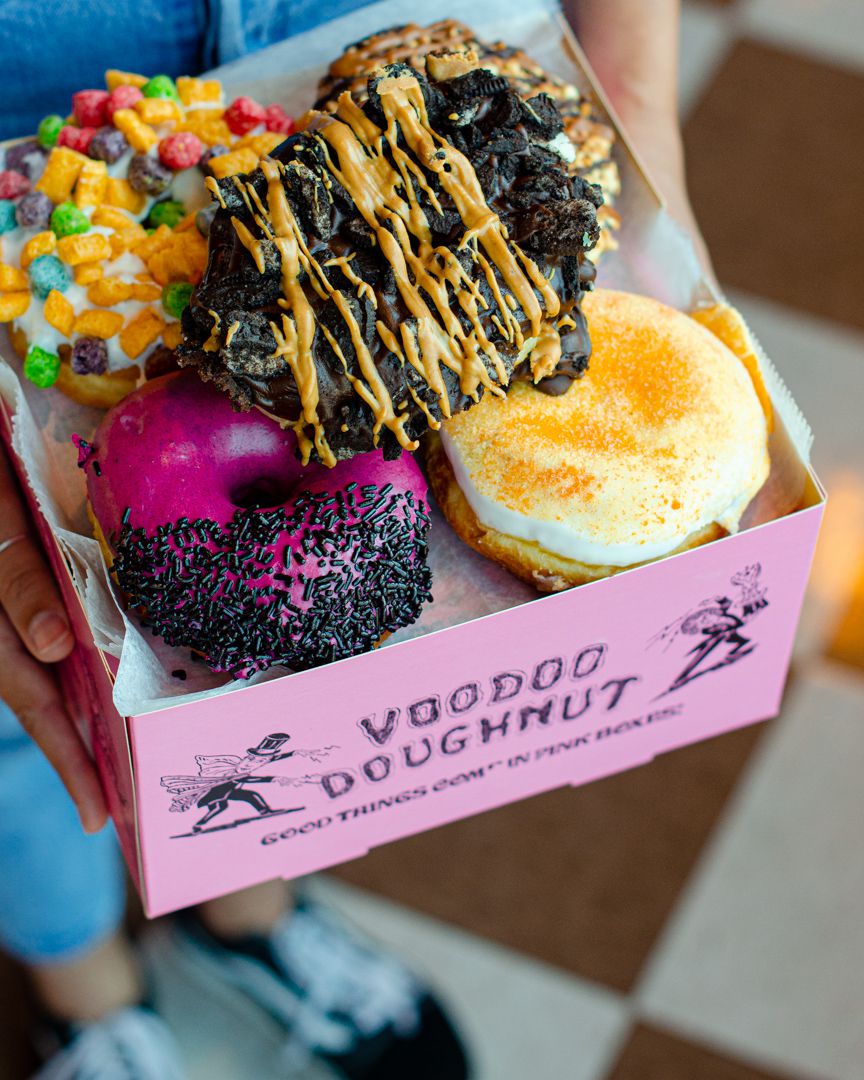 A Voodoo Doughnut box filled with a dozen frosted doughnuts.