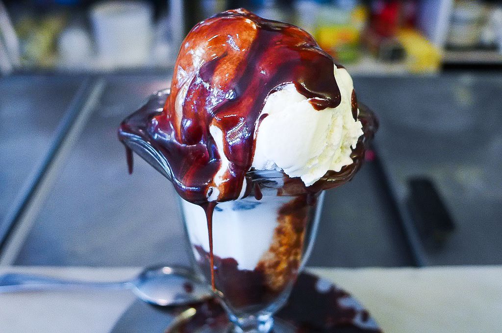 A tulip glass heaped with ice cream with hot fudge spilling down the sides.