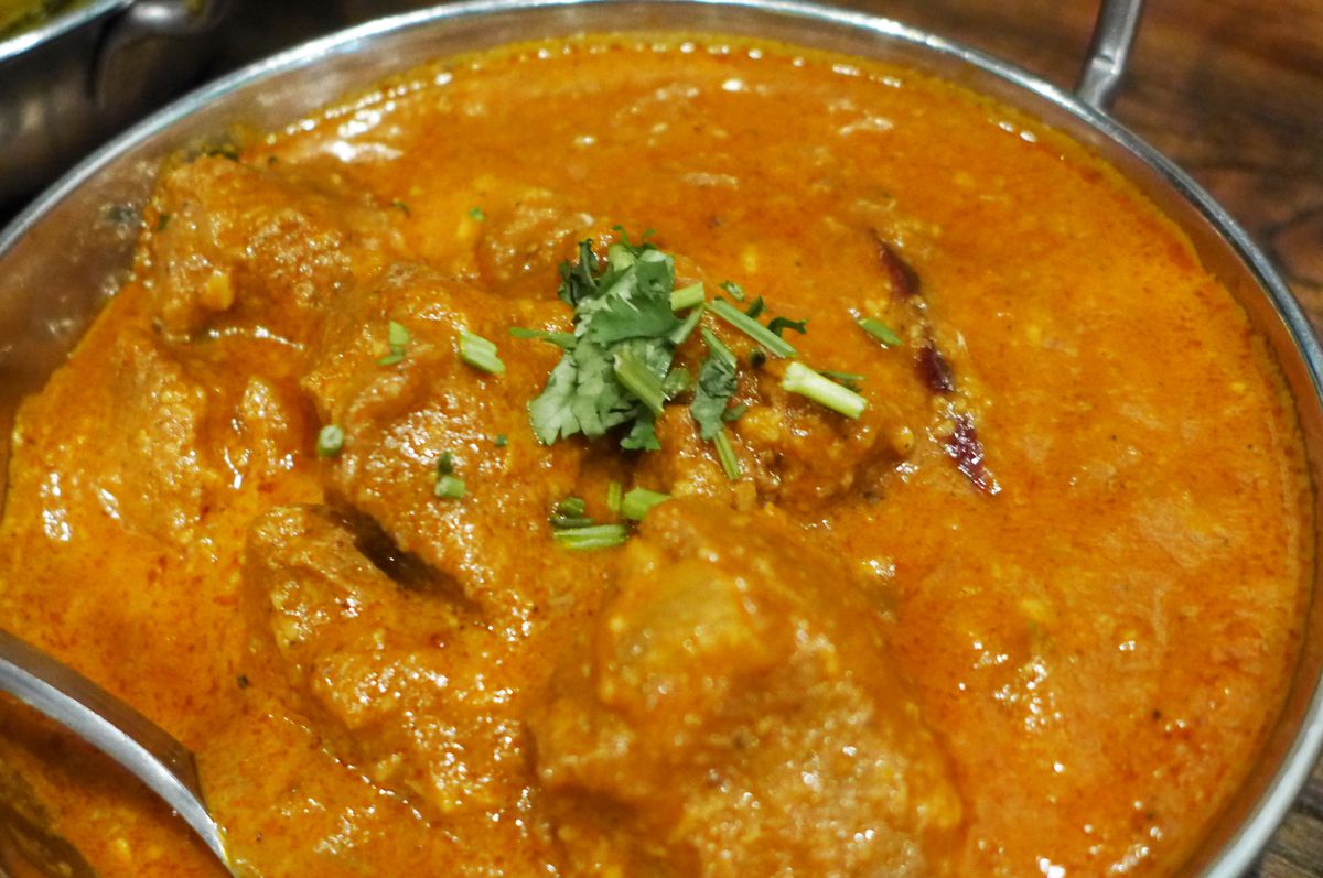 A chicken curry in a metal bowl with a yellowish cast.