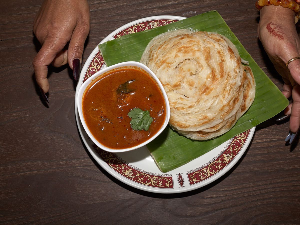 Fish curry with roti canai on banana leaf at Hawkers Kitchen, with a hand either side of the two plates