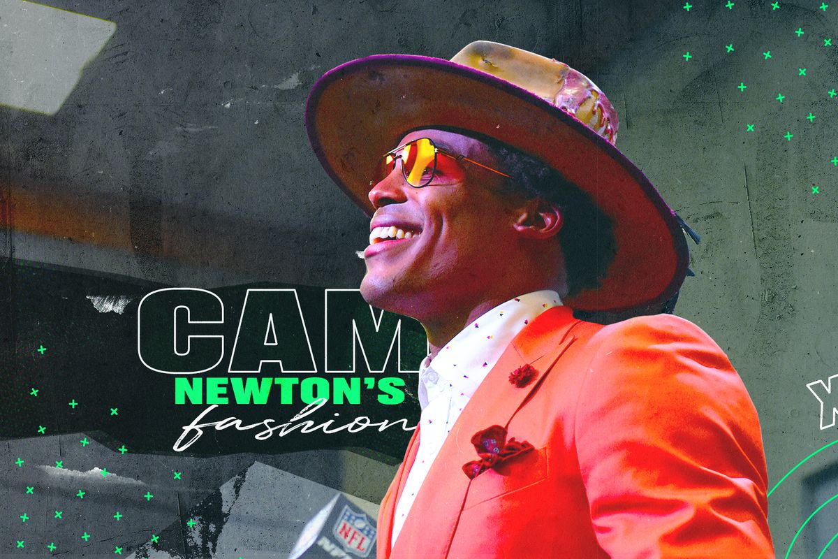 Cam Newton grins while wearing one of his fashionable post-game interview outfits: a bright orange suit, a polka-dot collared shirt, sunglasses, and a fedora.