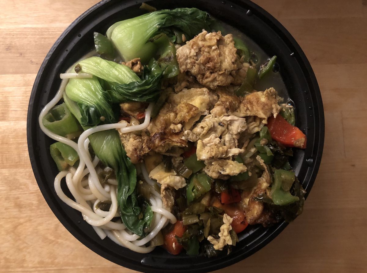 A black bowl of white noodles, green and red vegetables, and yellow scrambled eggs.
