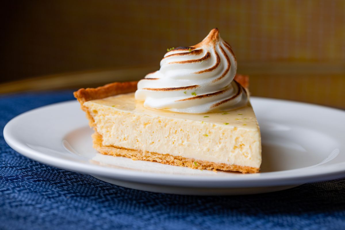 A side angle of a cut piece of creamy pie with whipped topping on a white plate and blue placemat at restaurant Denae’s.
