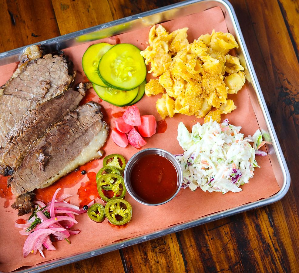 A silver tray with sliced brisket, pickled veggies, and coleslaw. 