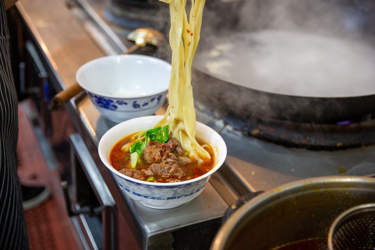 Beef noodle soup with noodles being lifted out of bowl