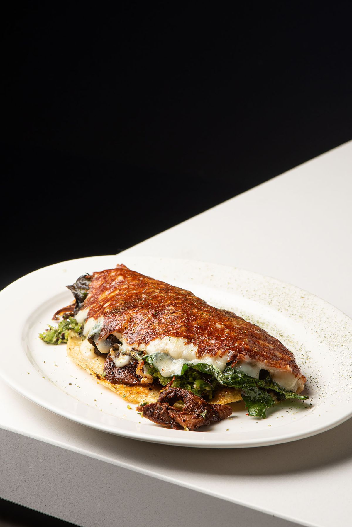 A large, messy folded-over tortilla sits on a plate, with a crispy outer layer of browned cheese.