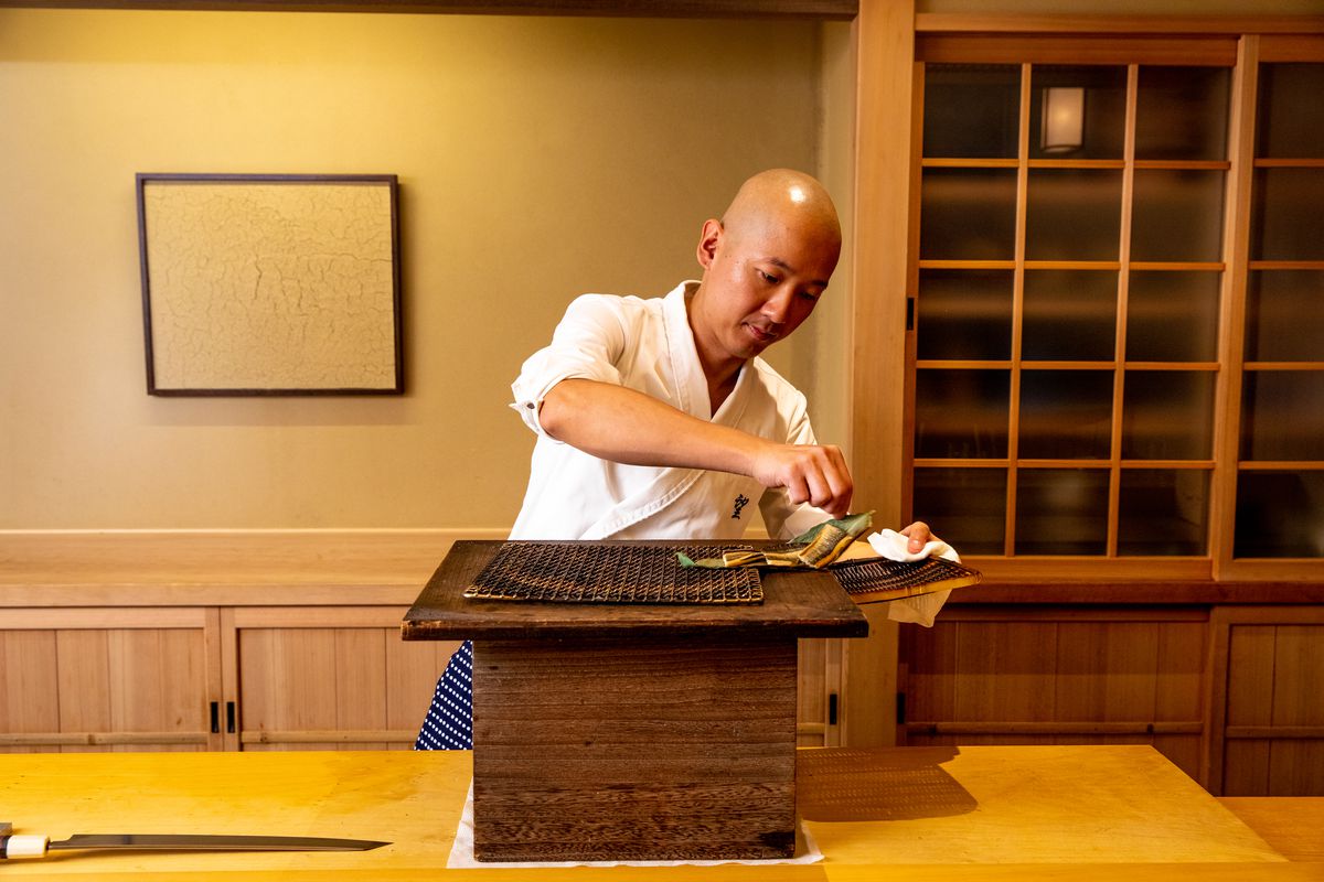 Chef Nozomu Abe pulls on a green bamboo leaf to remove sea eel from the binchotan grill