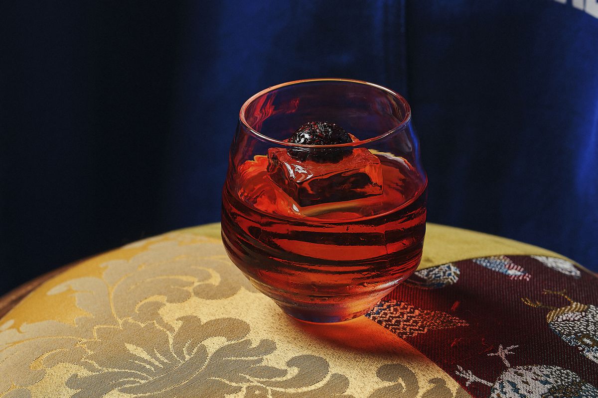 A red-hued cocktail in a glass with ice and topped with a raspberry
