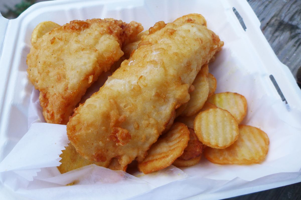 Two big pieces of battered fish and cottage fries in a Styrofoam container.