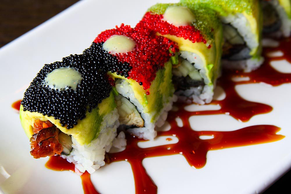 Four pieces of sushi on a white plate topped with slices of avocado and black and red roe. 