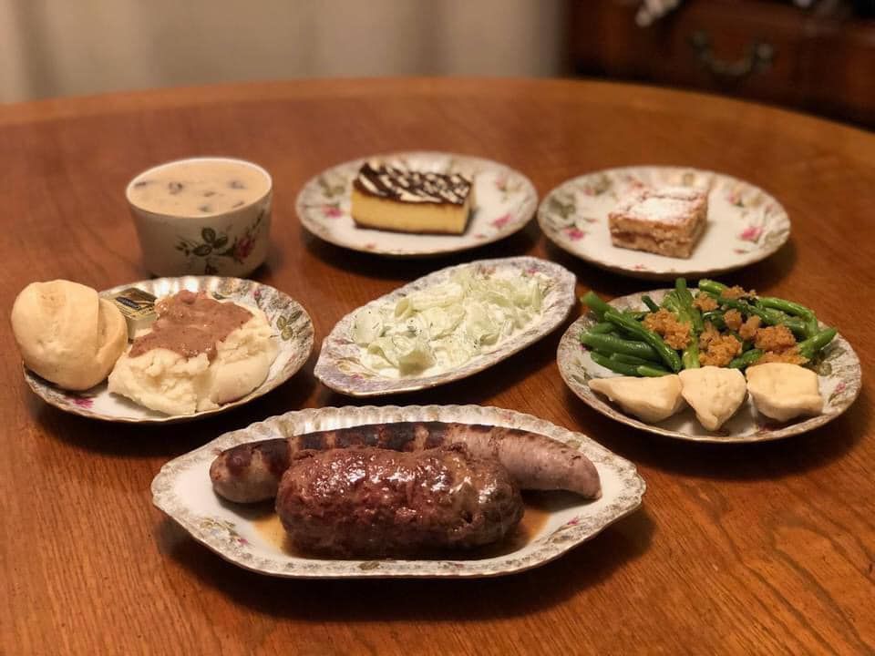 A table with dishes including beef roulade, Polish sausage, pierogi, cucumber salad, mushroom soup, green beans, mashed potatoes, cheesecake and apple cake