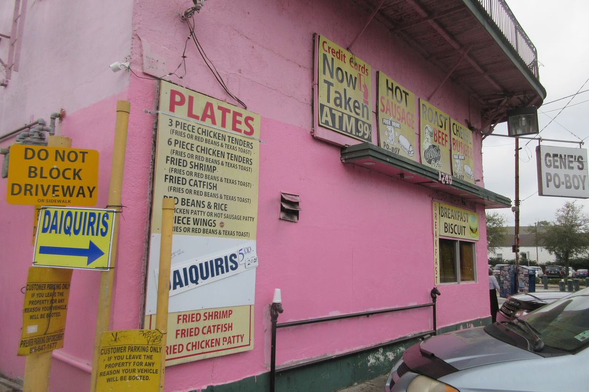 Several yellow signs advertising daiquiris and plate lunches are affixed to a bright-pink building.